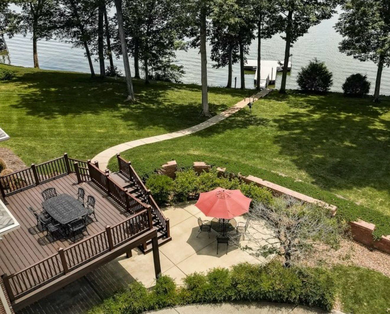 Backyard deck and patio with a red umbrella, and a winding path across the lawn to a private dock on the lake